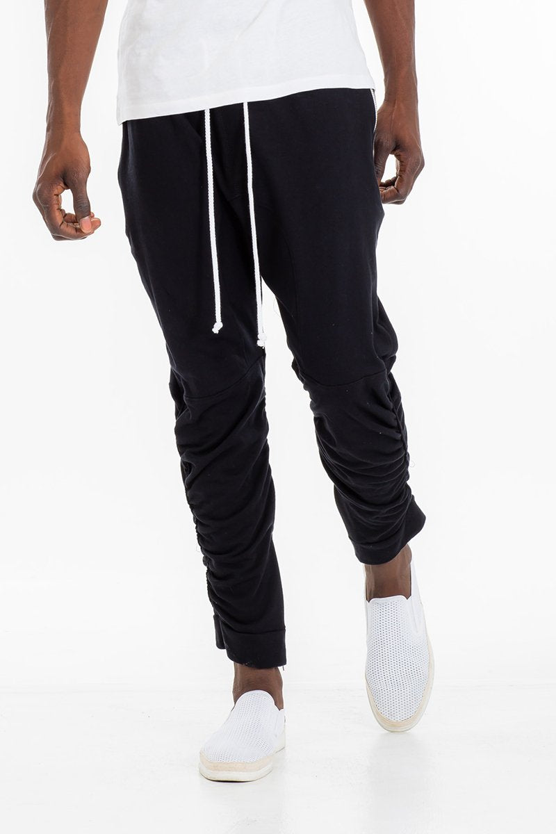 Person wearing black jogger pants with a white top on a white background