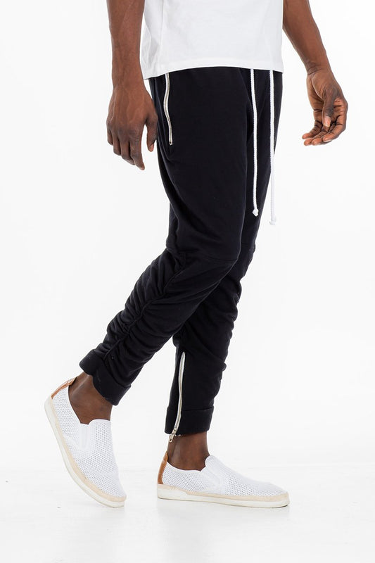 Person wearing black jogger pants with white stripes and white sneakers on a white background